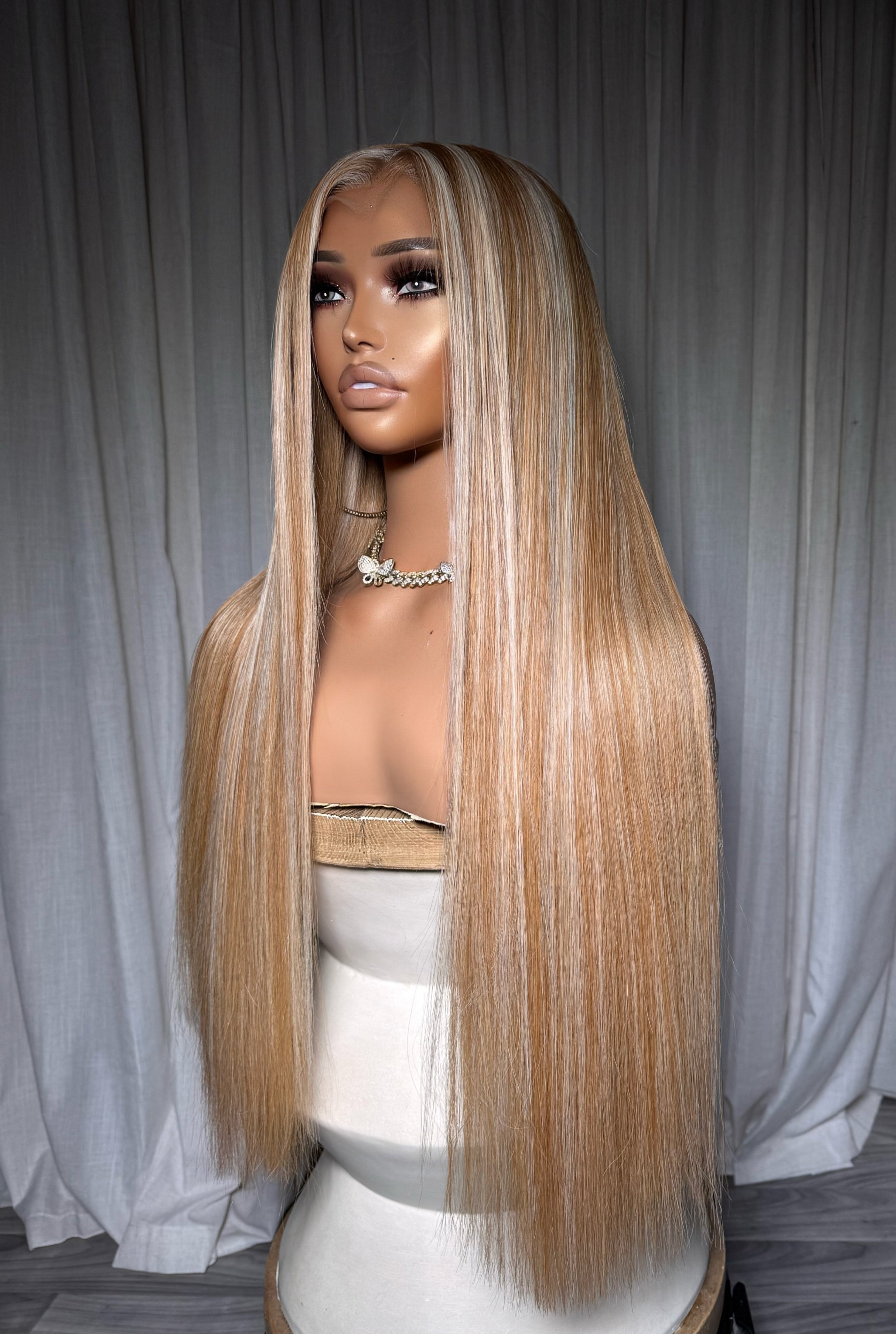 Mannequin head with long blonde wig against a gray curtain background