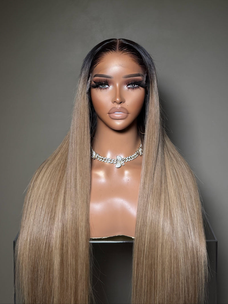 A long, straight wig with a dark root and a warm blonde ombré length, displayed on a mannequin bust against a dark gray background with the 'Empressly Glam' logo above.